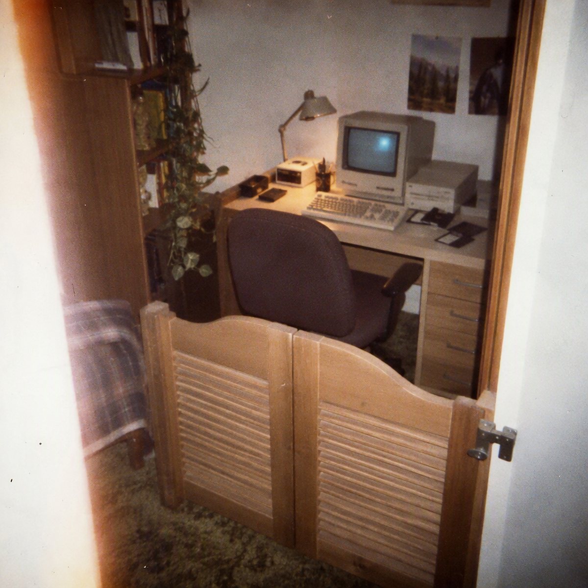 Wooden swinging half doors frame a small office containing a computer, desk, chair, lamp, and shelves.